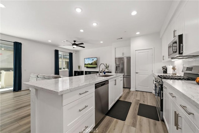 kitchen with light stone counters, an island with sink, white cabinets, and appliances with stainless steel finishes