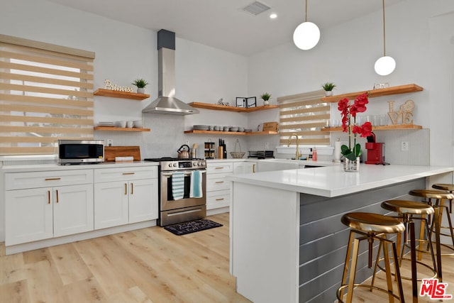 kitchen featuring tasteful backsplash, wall chimney range hood, pendant lighting, stainless steel appliances, and white cabinets