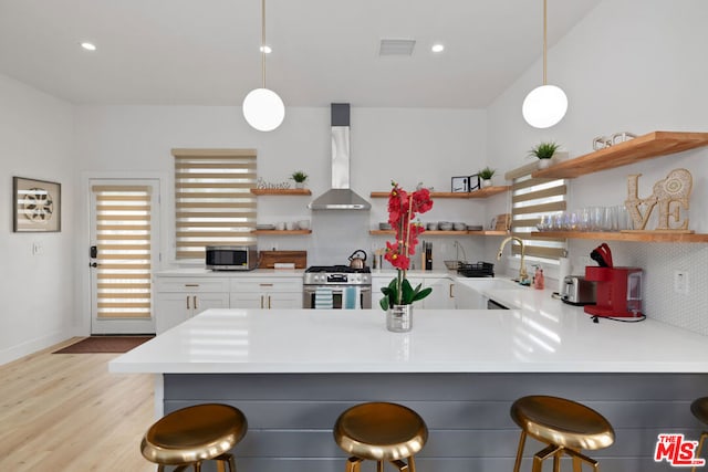 kitchen with appliances with stainless steel finishes, decorative light fixtures, wall chimney range hood, tasteful backsplash, and a kitchen breakfast bar