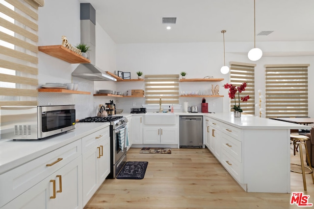 kitchen featuring a kitchen bar, stainless steel appliances, range hood, pendant lighting, and white cabinets