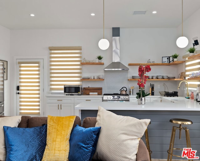 kitchen with decorative light fixtures, a kitchen bar, kitchen peninsula, white cabinetry, and wall chimney exhaust hood