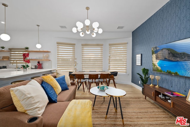 living room with a healthy amount of sunlight, sink, an inviting chandelier, and light hardwood / wood-style flooring