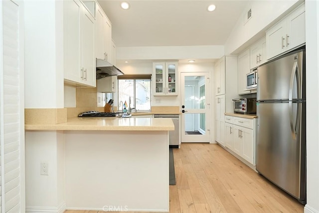 kitchen featuring light wood-type flooring, kitchen peninsula, stainless steel appliances, and white cabinetry