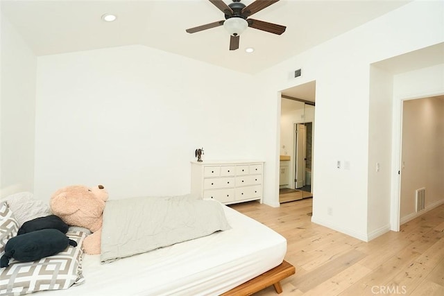 bedroom featuring ceiling fan, ensuite bathroom, lofted ceiling, and light wood-type flooring