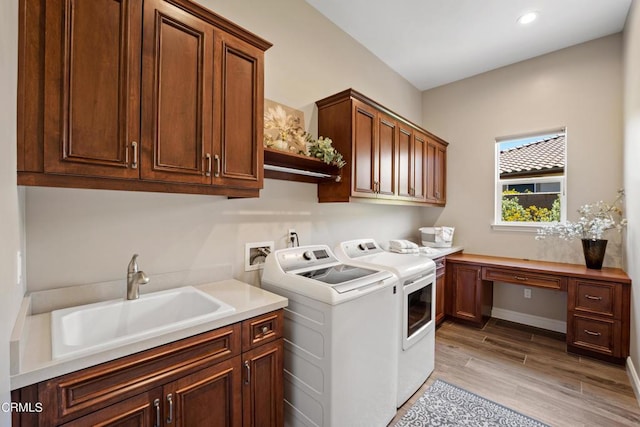 clothes washing area with cabinets, sink, separate washer and dryer, and light hardwood / wood-style flooring