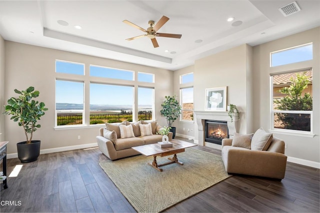 living room featuring ceiling fan, dark wood-type flooring, and a raised ceiling