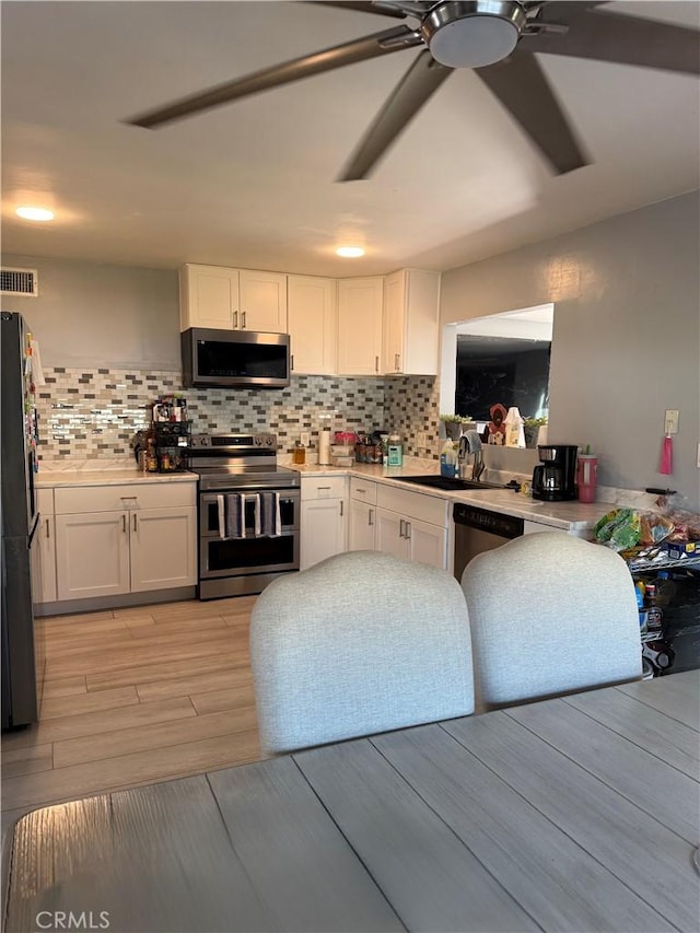 kitchen with sink, white cabinetry, light hardwood / wood-style flooring, appliances with stainless steel finishes, and decorative backsplash