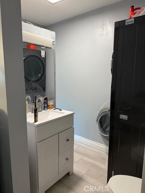 bathroom with vanity, stacked washer / drying machine, wood-type flooring, and toilet