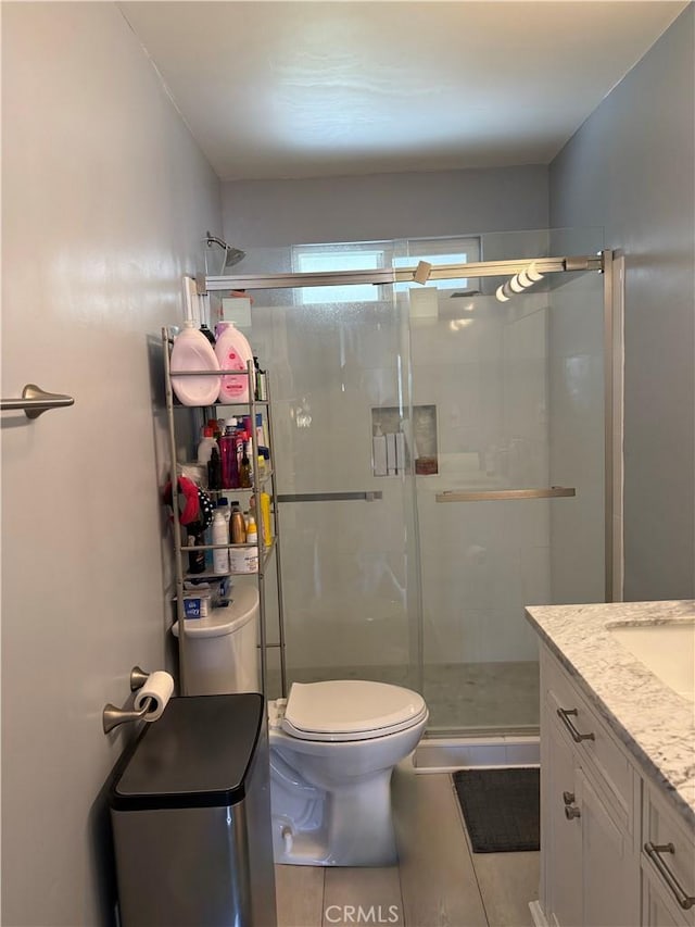 bathroom with a shower with door, vanity, tile patterned floors, and toilet