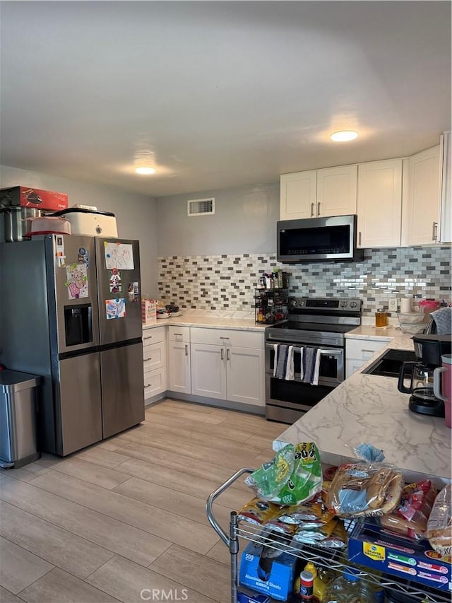 kitchen featuring tasteful backsplash, light hardwood / wood-style floors, white cabinets, and appliances with stainless steel finishes