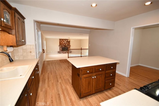 kitchen with a fireplace, a kitchen island, decorative backsplash, sink, and light wood-type flooring