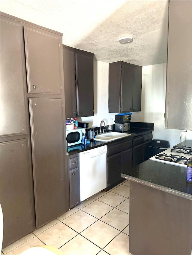 kitchen featuring dishwasher, sink, a textured ceiling, light tile patterned floors, and dark brown cabinets