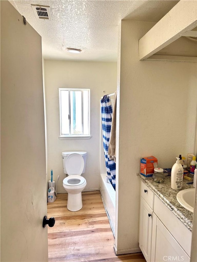 full bathroom featuring toilet, hardwood / wood-style floors, shower / bathtub combination with curtain, a textured ceiling, and vanity