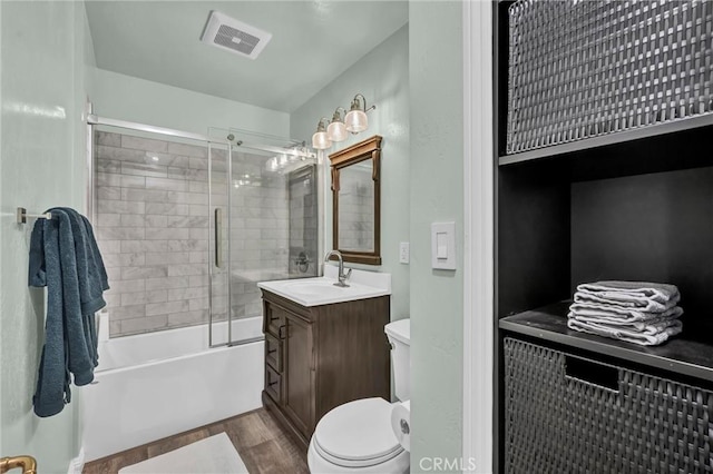 full bathroom featuring hardwood / wood-style flooring, enclosed tub / shower combo, vanity, and toilet