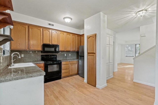 kitchen featuring black appliances, light wood-type flooring, backsplash, and sink