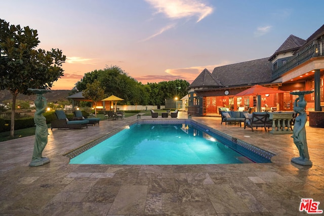 pool at dusk featuring an outdoor hangout area and a patio