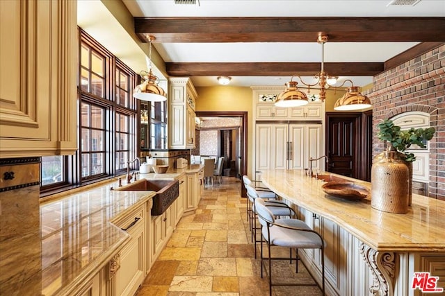 kitchen featuring decorative light fixtures, a breakfast bar, sink, beamed ceiling, and cream cabinetry