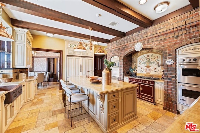 kitchen with pendant lighting, stainless steel double oven, range with two ovens, beamed ceiling, and a center island with sink