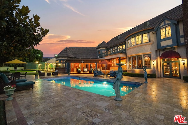 pool at dusk with french doors and a patio