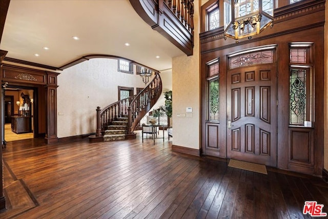 entryway with dark wood-type flooring, a wealth of natural light, crown molding, and a towering ceiling