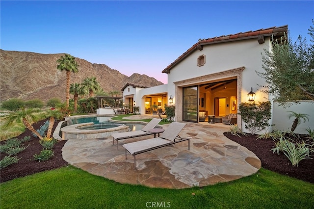 patio terrace at dusk featuring a mountain view and a pool with hot tub