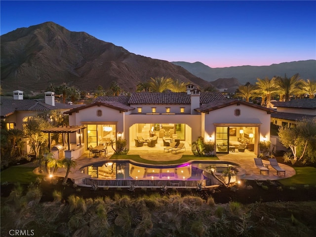 back house at dusk featuring a mountain view, a pergola, and a patio