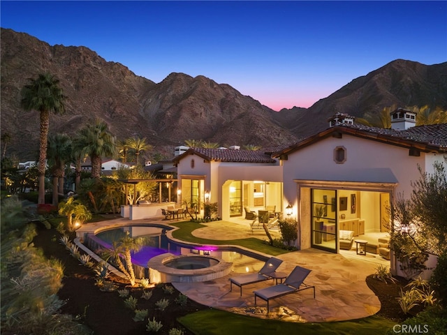 back house at dusk featuring a pool with hot tub, a mountain view, and a patio area