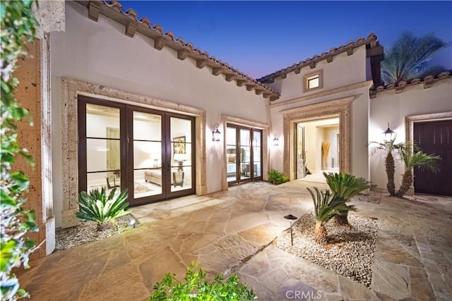 back house at dusk featuring french doors and a patio