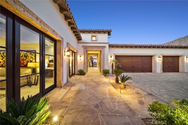 property entrance featuring a tile roof, decorative driveway, a garage, and stucco siding