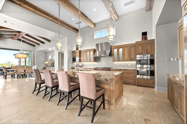 kitchen with wall chimney exhaust hood, a kitchen bar, a large island with sink, double oven, and pendant lighting