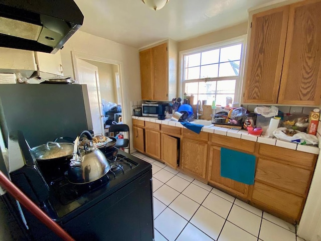 kitchen with black range, light tile patterned flooring, tile counters, and range hood