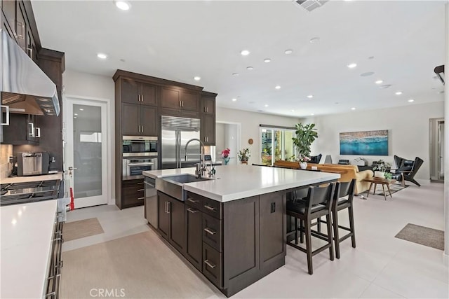 kitchen with range hood, stainless steel appliances, a sink, light countertops, and open floor plan