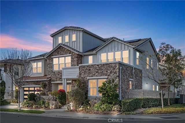 view of front of property featuring stone siding, board and batten siding, solar panels, and concrete driveway