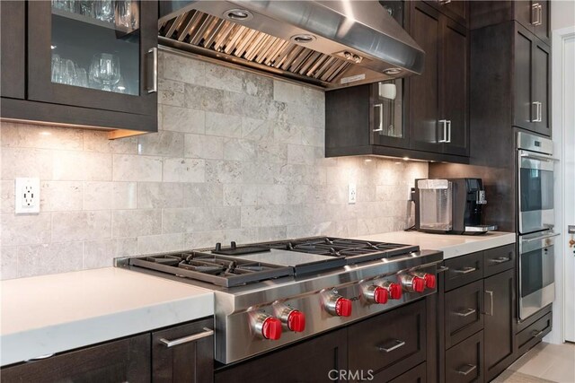 kitchen with tasteful backsplash, stainless steel appliances, dark brown cabinets, and wall chimney range hood