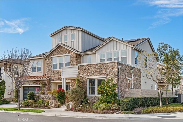 craftsman-style house with solar panels, board and batten siding, concrete driveway, and stone siding