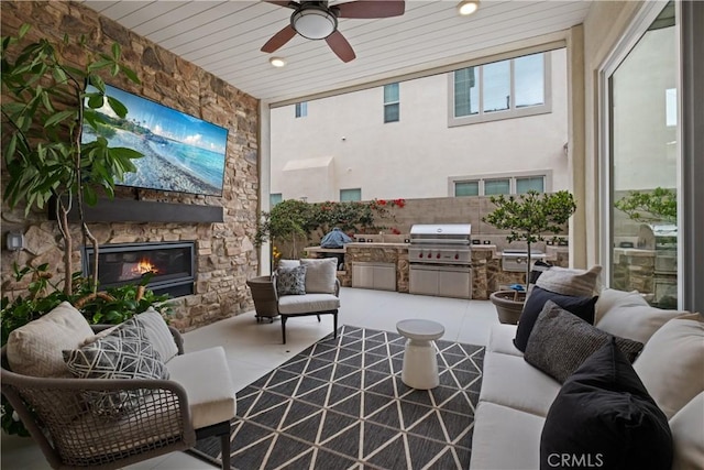 view of patio with fence, exterior kitchen, an outdoor living space with a fireplace, ceiling fan, and a grill