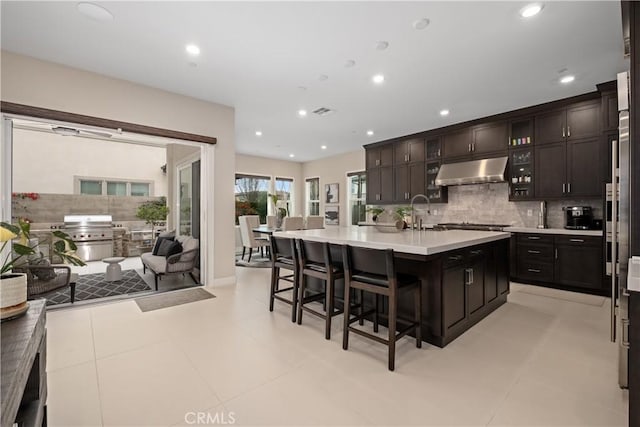 kitchen with a breakfast bar area, light countertops, under cabinet range hood, open floor plan, and backsplash