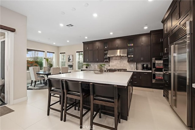 kitchen with visible vents, stainless steel built in refrigerator, under cabinet range hood, light countertops, and decorative backsplash