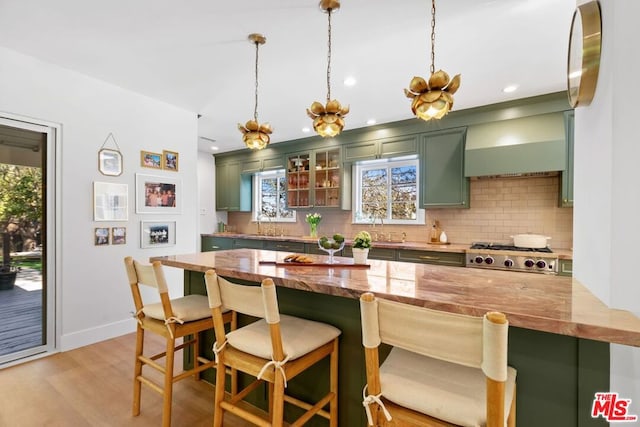 kitchen featuring kitchen peninsula, green cabinets, a kitchen breakfast bar, light wood-type flooring, and wall chimney range hood