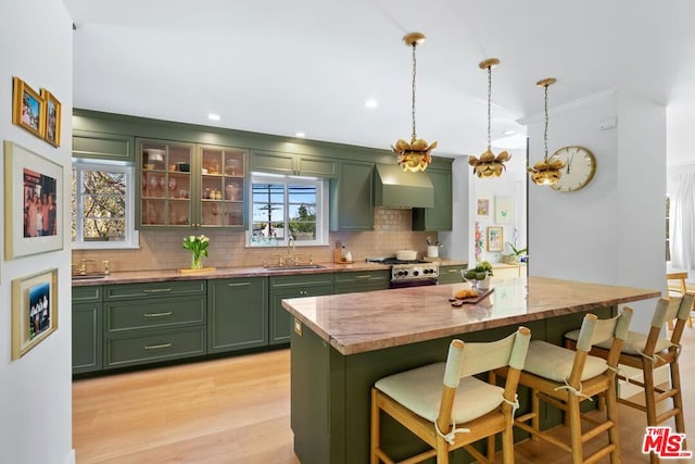 kitchen with wall chimney range hood, pendant lighting, a kitchen bar, sink, and green cabinetry