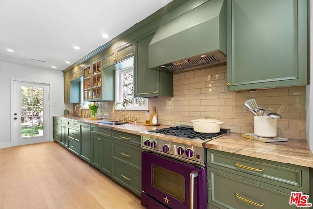 kitchen with sink, wall chimney exhaust hood, green cabinets, and range with gas cooktop