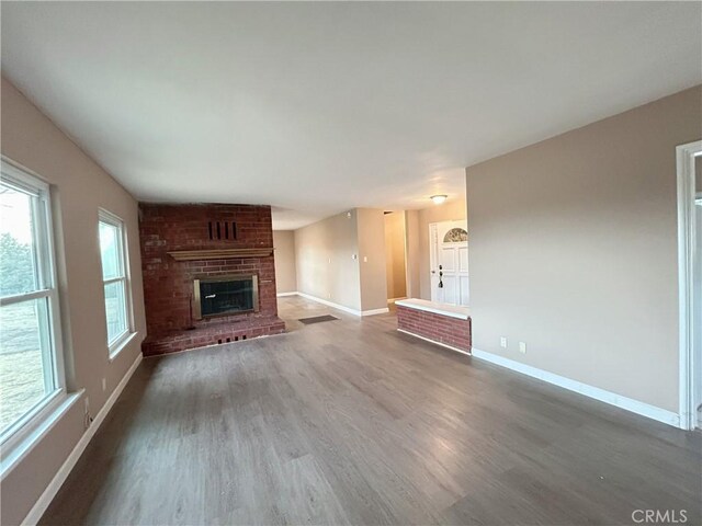 unfurnished living room featuring dark hardwood / wood-style flooring and a brick fireplace