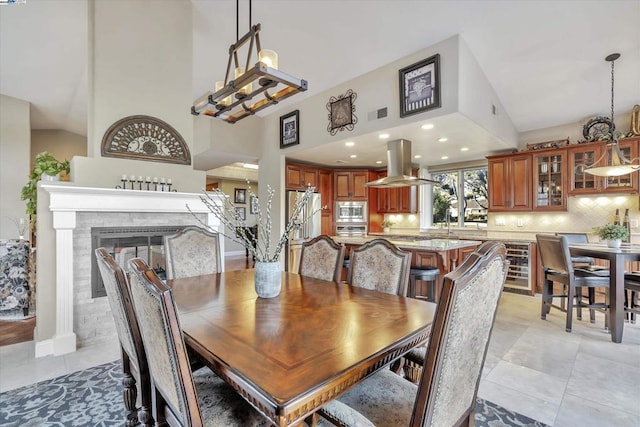 tiled dining area with a fireplace, sink, high vaulted ceiling, and beverage cooler