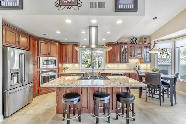 kitchen featuring appliances with stainless steel finishes, backsplash, light stone counters, a center island, and island range hood