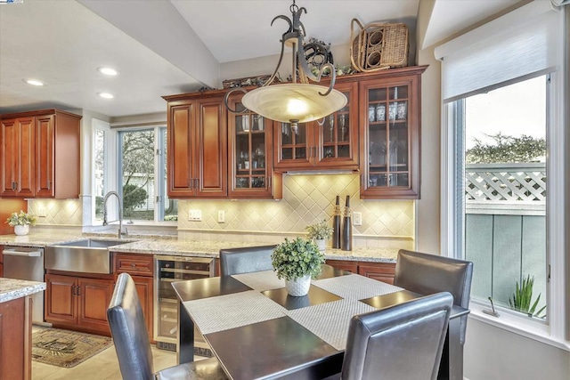 kitchen featuring hanging light fixtures, sink, backsplash, light stone counters, and beverage cooler