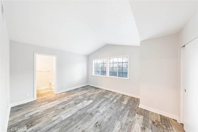 unfurnished bedroom featuring light wood-type flooring, a closet, vaulted ceiling, and connected bathroom