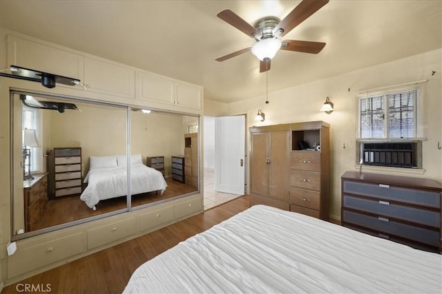 bedroom with light hardwood / wood-style floors, cooling unit, a closet, and ceiling fan