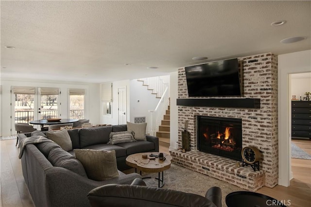 living room with a brick fireplace, light hardwood / wood-style floors, a textured ceiling, and french doors