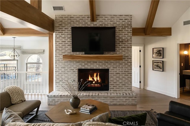 living room with a fireplace, beamed ceiling, an inviting chandelier, and hardwood / wood-style flooring