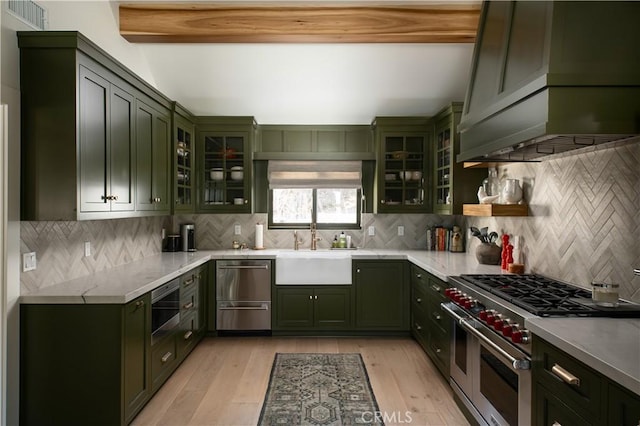 kitchen featuring island exhaust hood, green cabinets, appliances with stainless steel finishes, beam ceiling, and sink